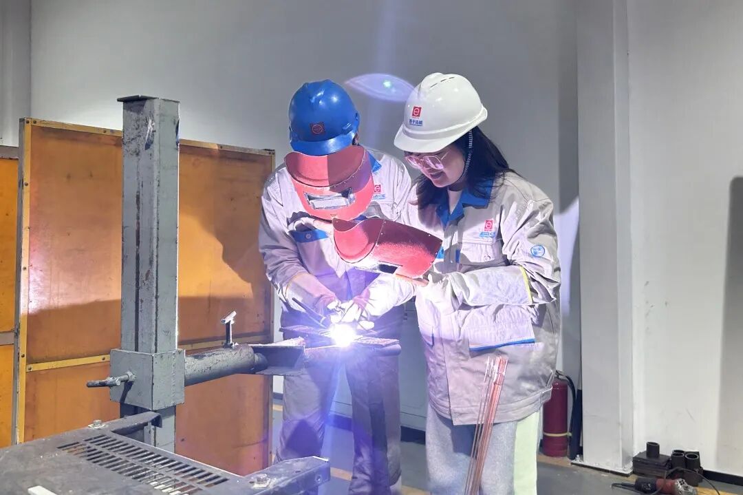 葛小青(左)指导记者手握焊枪进行焊接。 图片